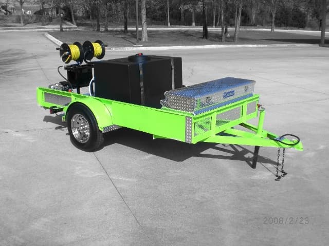 Green DB Series open utility trailer with a black water tank, twin yellow hose reels, and an aluminum toolbox on a single axle
