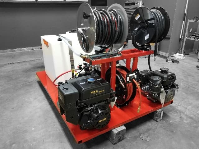 DVT skid unit with a red frame, poly tank, two hose reels, and two gas engines, resting on blocks in a shop