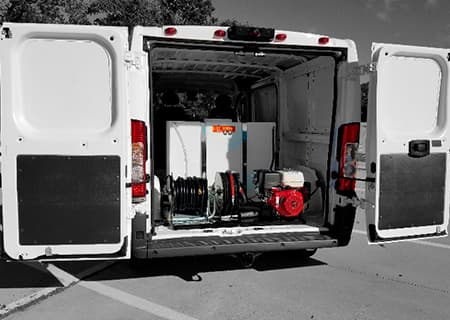 DVTP hot-water pressure washing skid mounted inside a white cargo van, rear doors open, hose reel and tank visible, parked in a lot
