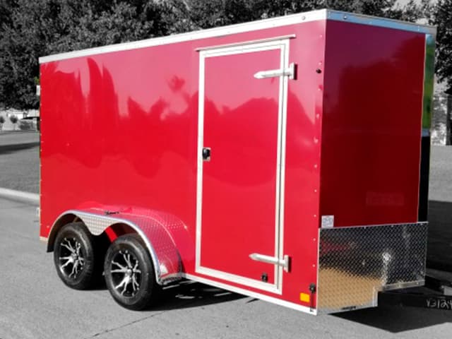 Red DE Series enclosed cargo trailer on a tandem axle with a side entry door, parked in a lot