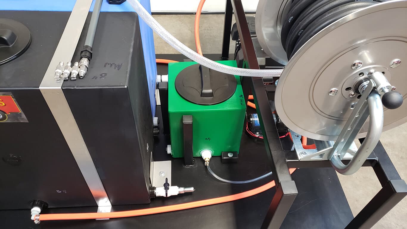 Soft wash skid unit with a black tank, green chemical box and chrome hose reel, staged in a shop